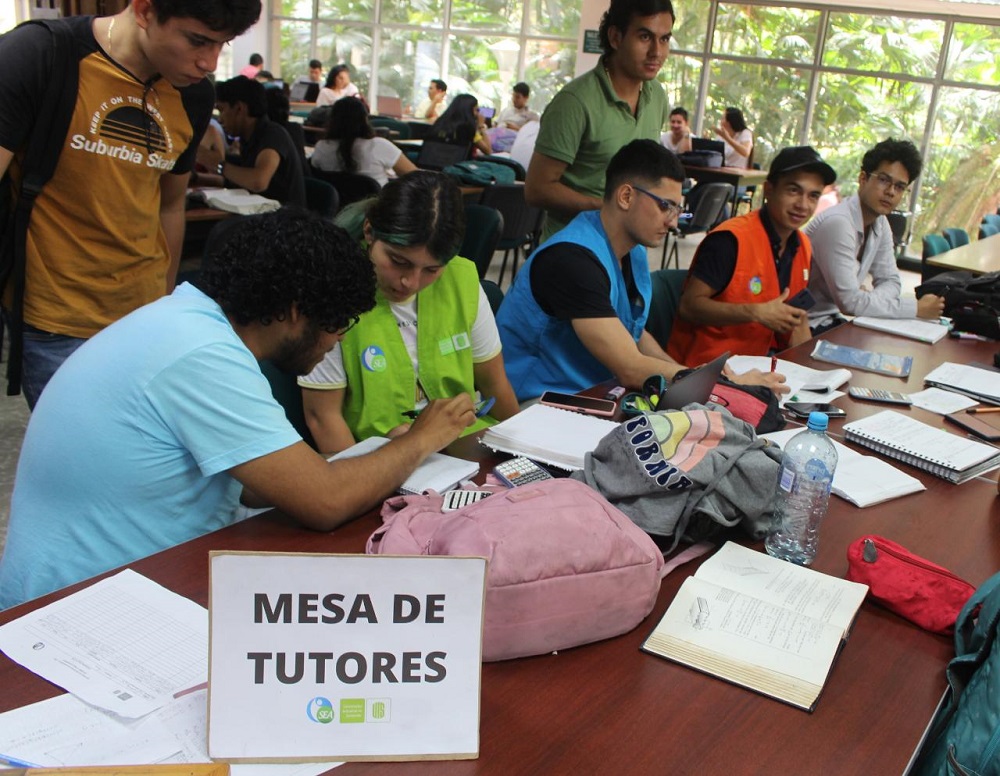 La foto muestra mesa de tutores y estudiantes en la Biblioteca