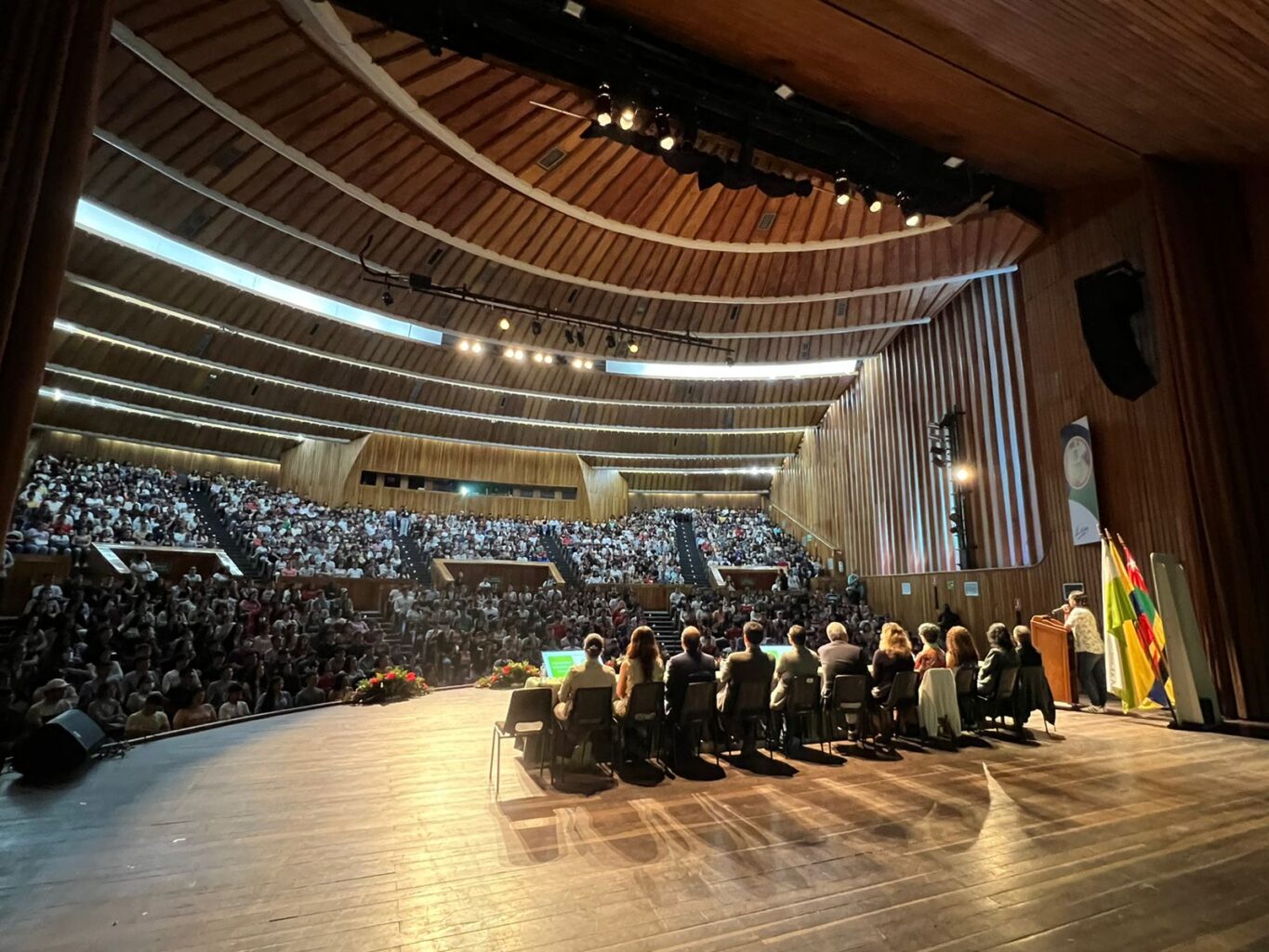 Imagen muestra al Consejo Académico de espaldas y al fondo el auditorio completamente lleno de estudiantes.  