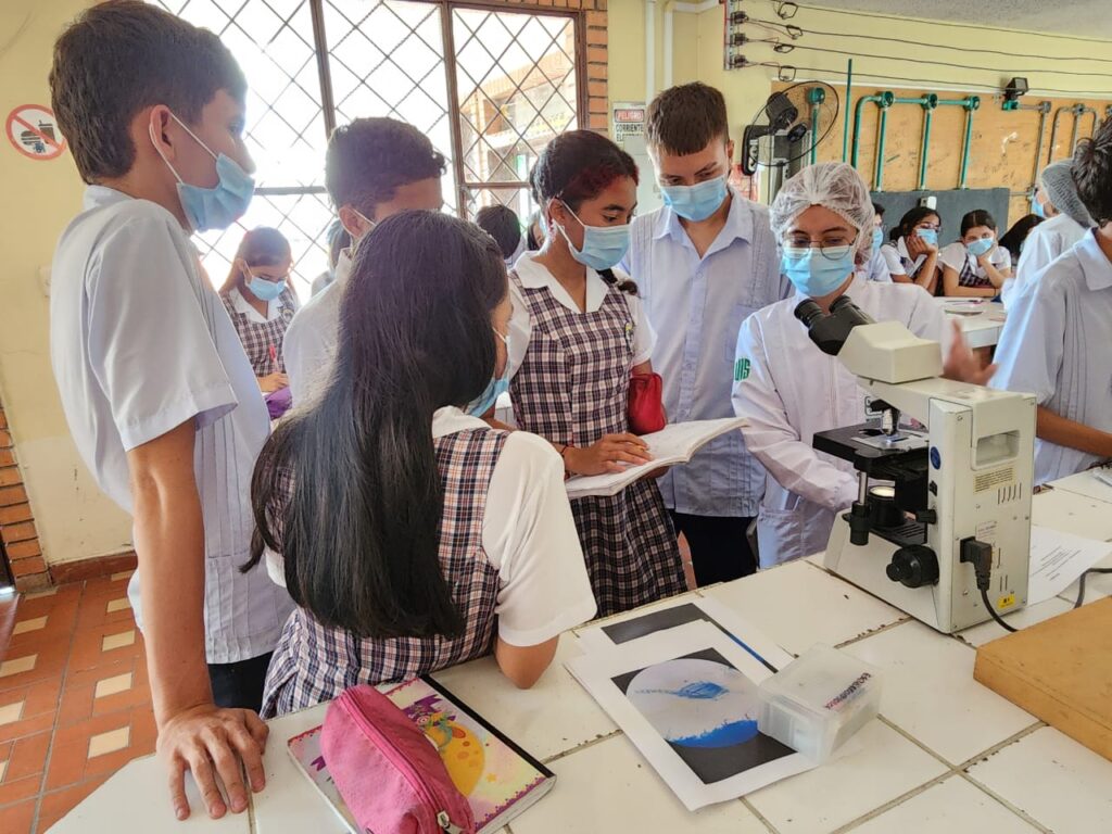 Estudiante UIS explicando el  uso del microscopio a los estudiantes del Instituto