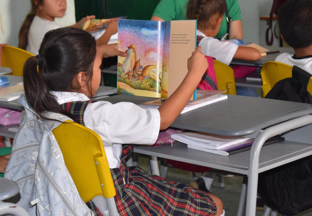 Niña con libro en sus manos dentro de un salón de clase